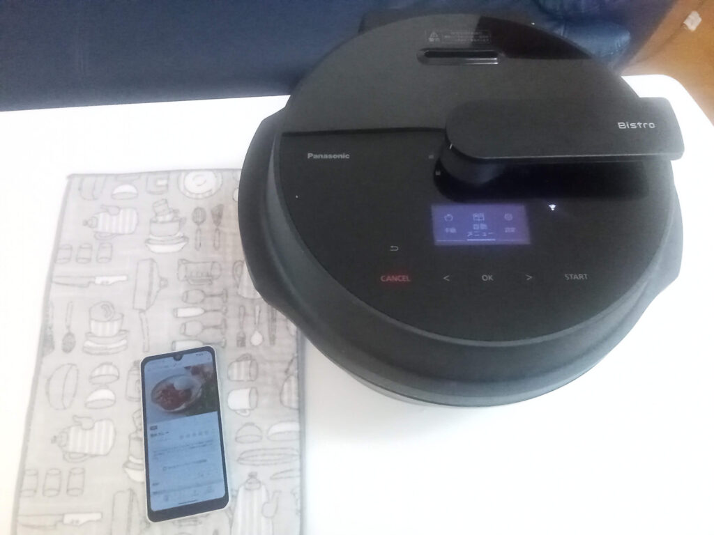 オートクッカービストロの横に置いた、キッチンポケットアプリのレシピ画面を表示するスマートフォン