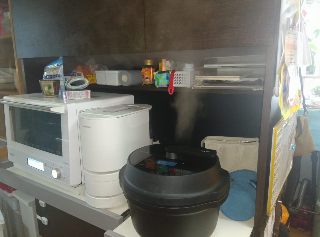 炊飯器の隣でオートクッカービストロNF-AC1000を使い蒸気が上の棚板へ当たる様子